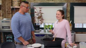 Martin in a blue jumper and Kate in a pink jumper in a kitchen preparing arthritis-friendly recipes