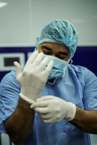 Surgeon wearing a mask and scrubs, putting on gloves.
