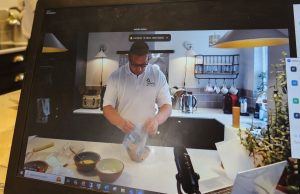 Arthritis Action Dietitian demonstrating a recipe, during filming of a cook-a-long charity event. Martin is pouring ingredients in a bowl, in a home kitchen, wearing a white shirt with Arthritis Action logo.