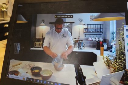 Arthritis Action Dietitian demonstrating a recipe, during filming of a cook-a-long charity event. Martin is pouring ingredients in a bowl, in a home kitchen, wearing a white shirt with Arthritis Action logo.